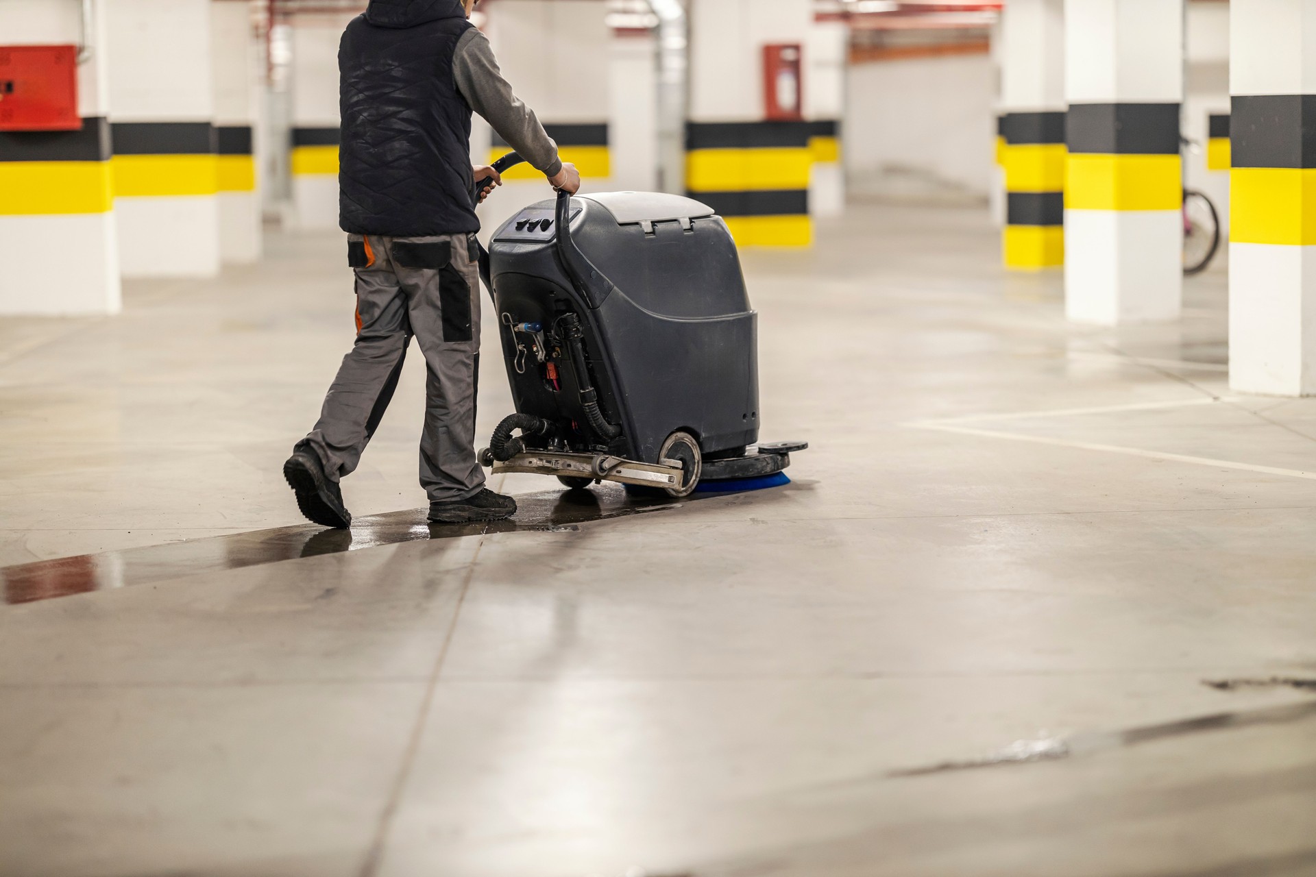 Rear view of worker using scrubber machine for cleaning garage.